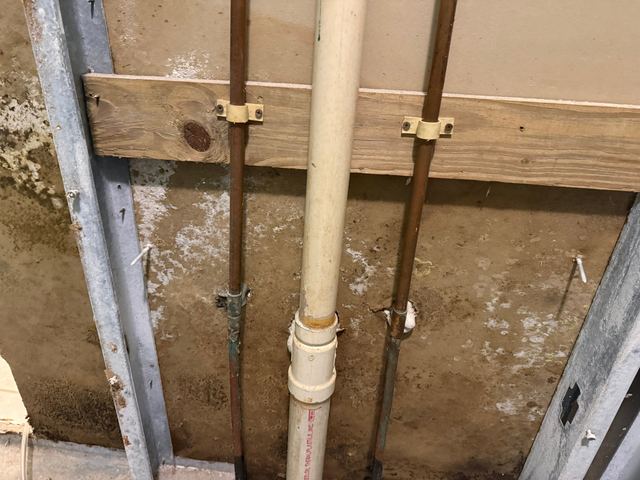 Mold-stained wall cavity with pipes in an opened bathroom wall, and the same bathroom with drying equipment running.